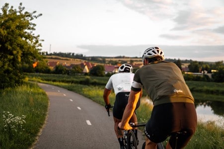 Two clyclists riding on a narrow, country road. They are both wearing road cycling gear.