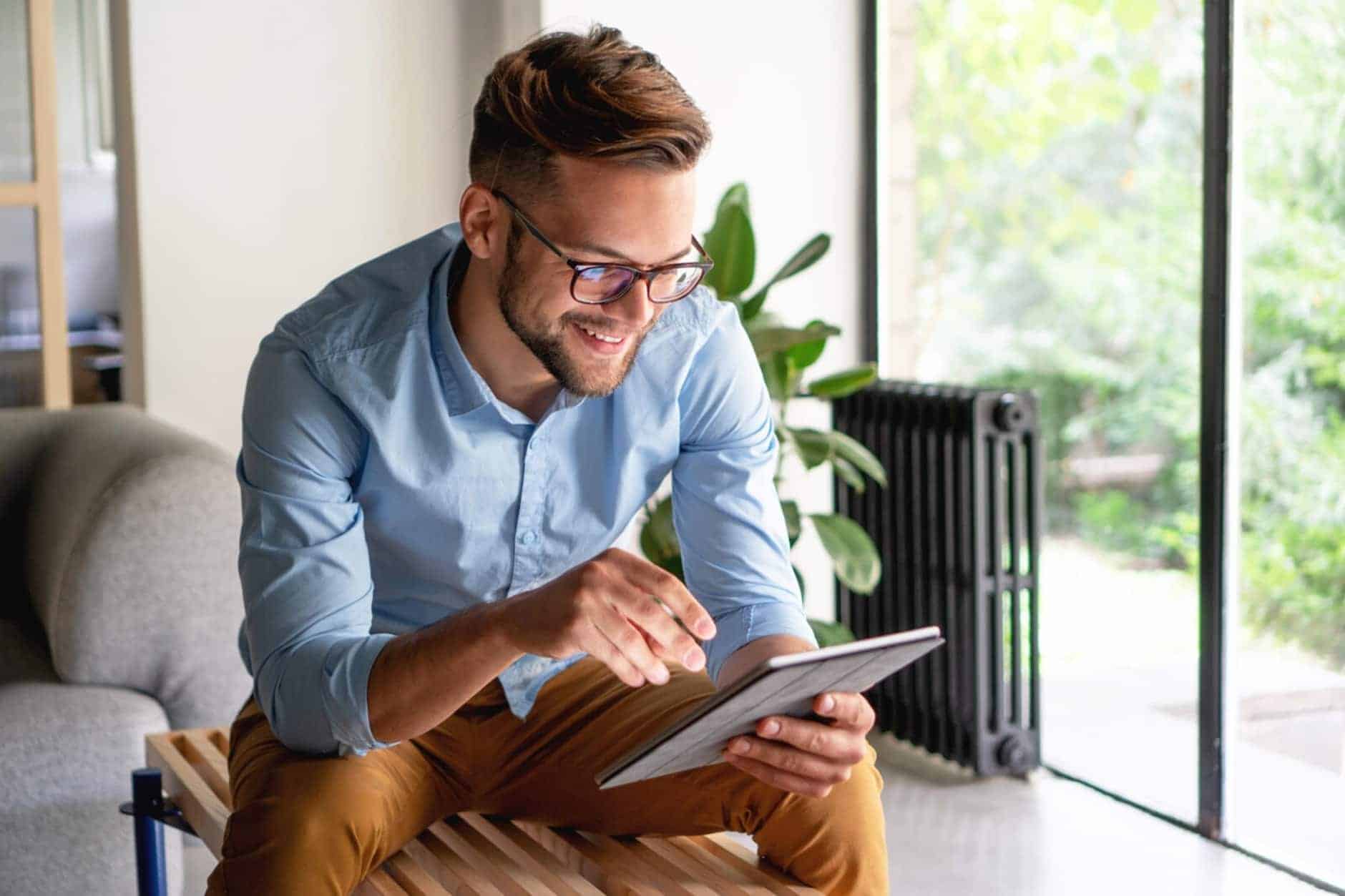 A man sitting on a wooden bench smiling while looking at his tablet.