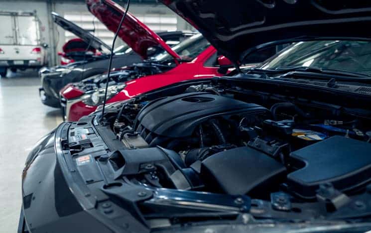 A row of cars in a garage with their bonnets open being worked on