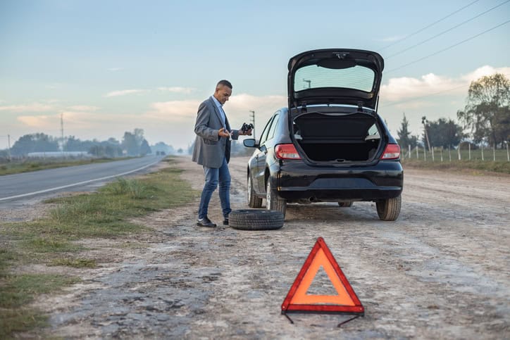 Confused latino man tries to change the flat tire of his car with copy space.