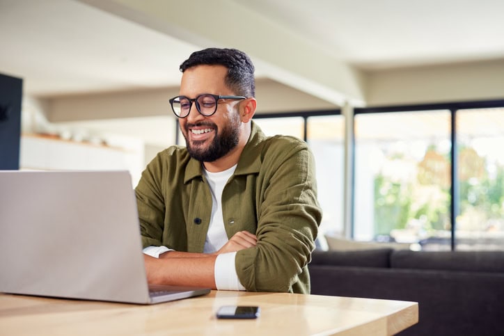 Happy hispanic man working on laptop at home