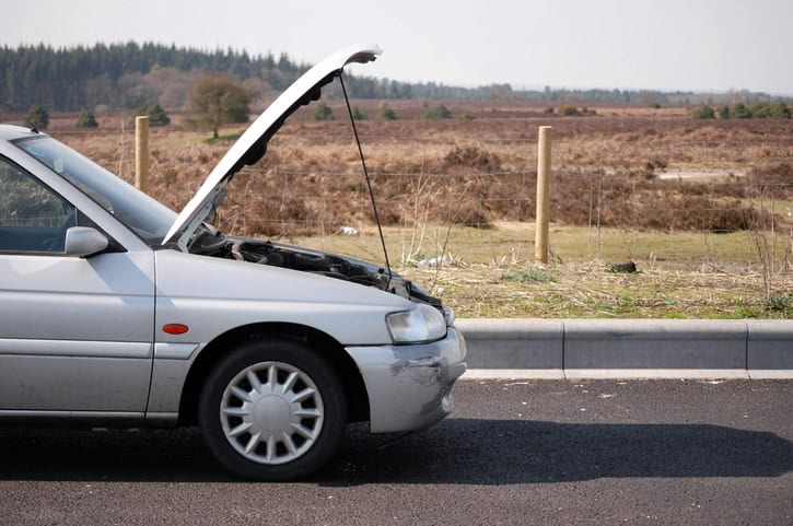 A gray car with its hood open parked by the side of the road