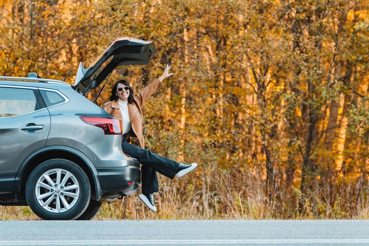 A smiling woman sits in the trunk of a car