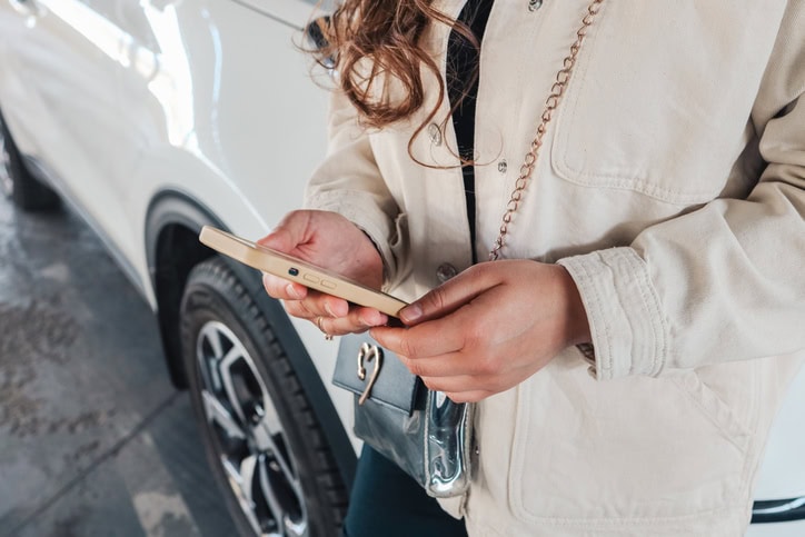 Woman using a phone in front of a car