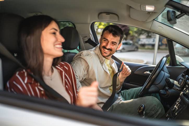 Happy adult man driving a car accompanied by his girlfriend