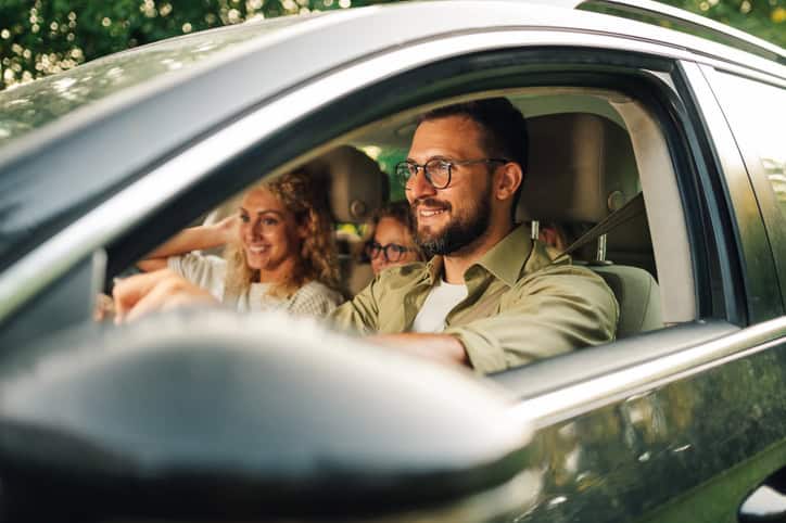 Image of a father with his family in a black car driving along a road