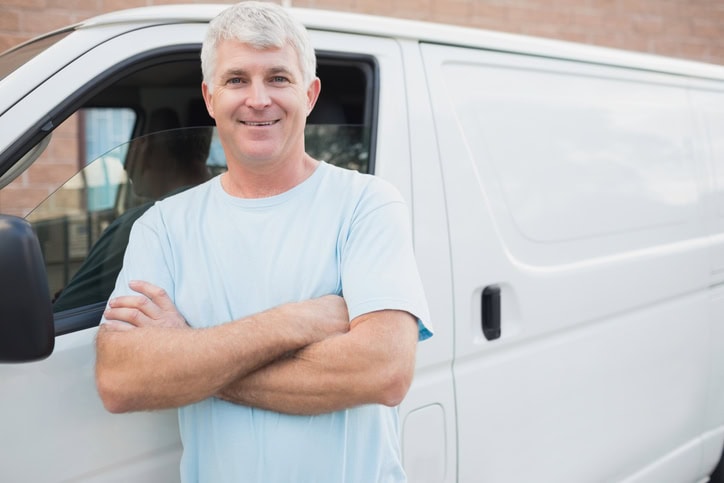 An older man standing outside a white van smiling