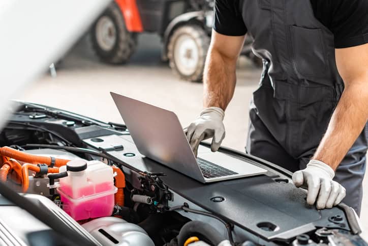 Cropped view of mechanic using laptop near car engine compartment