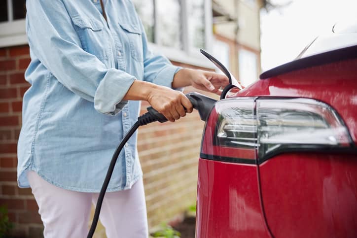 A woman in a button shirt charging a red car